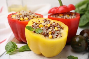 Quinoa stuffed bell peppers, basil and tomatoes on white table, closeup