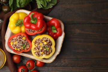 Quinoa stuffed bell peppers in baking dish, basil and tomatoes on wooden table, flat lay. Space for text