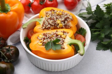 Quinoa stuffed bell pepper, tomatoes and parsley in bowl on light table, closeup