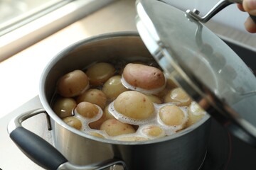 Boiling potatoes in pot on stove in kitchen, closeup