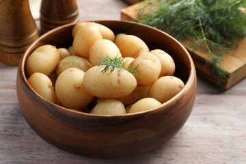 Boiled potatoes in bowl and dill on wooden table, closeup