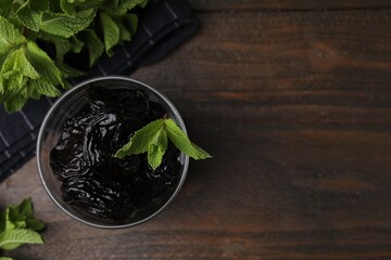 Tasty dried plums (prunes) in glass bowl and mint leaves on wooden table, flat lay. Space for text