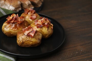 Delicious baked potatoes with bacon on wooden table, closeup. Space for text