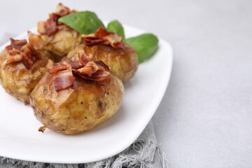 Delicious baked potatoes with bacon and basil on grey table, closeup. Space for text