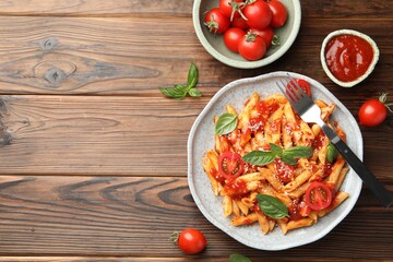 Delicious pasta with tomato sauce, basil and cheese served on wooden table, flat lay. Space for text