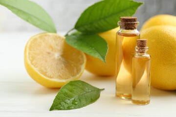 Essential oils in bottles, lemons and green leaves on white table