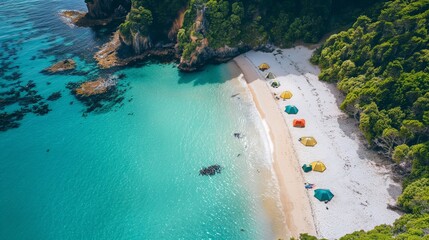 The beach from above showcases a stunning mosaic of tents against the vivid backdrop of emerald waters and lush green cliffs.