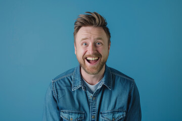 Obraz premium a Caucasian man in a blue denim shirt, showing happiness with a big smile on a blue studio background