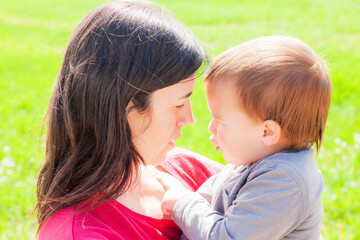 Tender glance between a mother and child beside a green meadow. Motherhood.