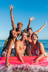 Vertical group of young friends having fun at the beach, floating on an inflatable mattress by the...