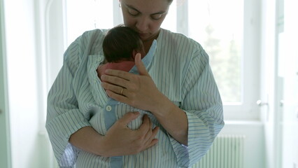Mother holding newborn baby close to her chest, wrapped in a striped hospital gown, capturing the...