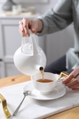 Woman pouring hot tea into cup at wooden table, closeup
