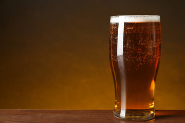 Glass with fresh beer on wooden table against dark background, closeup. Space for text