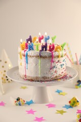 Tasty Birthday cake with burning candles and party decor on white table