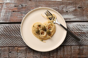 Heart made of tasty spaghetti, fork, olives and cheese on wooden table, top view