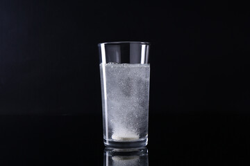 Effervescent pill dissolving in glass of water on black background