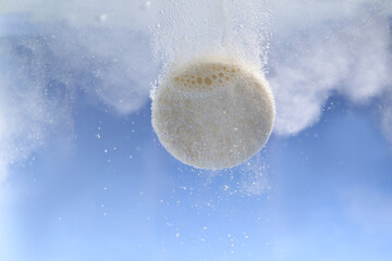 Effervescent pill dissolving in water on light blue background, closeup