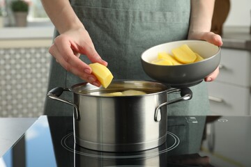 Woman putting potato into saucepan on stove, closeup