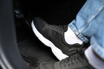 Man in sneakers pushing on pedal of car brake, closeup