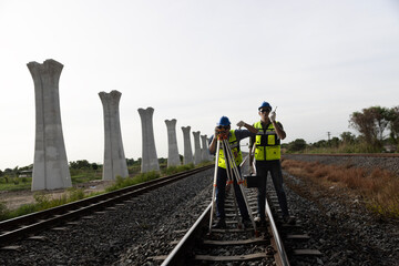 Two male railway technicians using theodolite surveying optical instruments and a coworker holding...