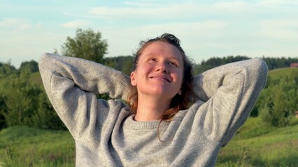 Young carefree happy woman walking at summer day at nature, enjoy good weather, deep breath fresh air and raise her arms 