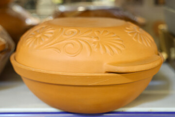A large orange pot with a floral design sits on a shelf