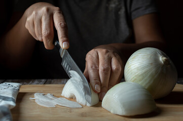 Concept of taking or grabbing food with hands, feminine Mexican hands. julienne cut onion on a wooden cutting board. Horizontal front view dark mood image