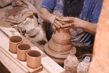 Wet hands of a male potter sculpting clay and shaping a vase on a potter's wheel.