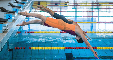 Two professional female swimmers taking track start position on the platform gracefully jumping and...