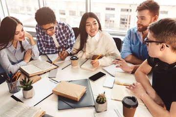 Students in library sharing information and preparing for exam with books on desk