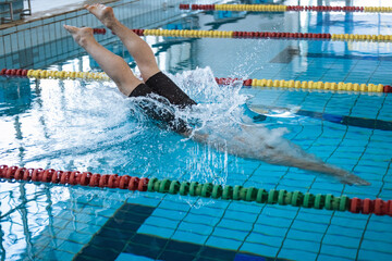 Male swimmer jumping off the starting block into the pool. Concept of determination and competitive sport.