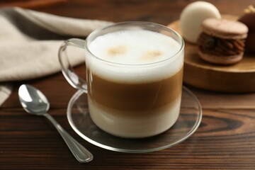 Aromatic coffee in cup, spoon and macarons on wooden table, closeup