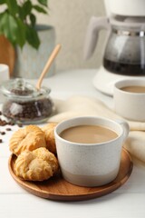 Aromatic coffee in cup and tasty profiteroles on white wooden table