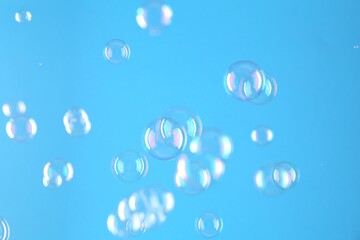 Beautiful transparent soap bubbles on light blue background