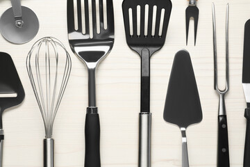 Different spatulas and other kitchen utensils on light wooden table, flat lay