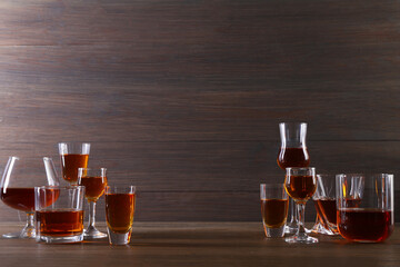Different delicious liqueurs in glasses on wooden table, space for text