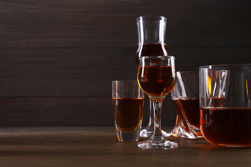 Different delicious liqueurs in glasses on wooden table, space for text