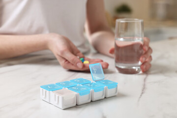 Fototapeta premium Woman with pills, organizer and glass of water at white marble table, selective focus