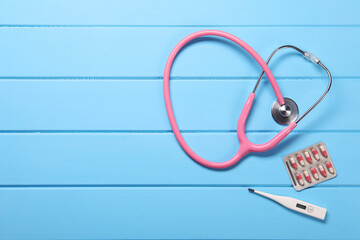 Stethoscope, thermometer and pills on light blue wooden background, flat lay. Space for text