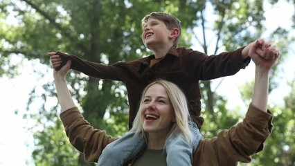Stylish and happy european mother with son on shoulders at outdoor in summer time