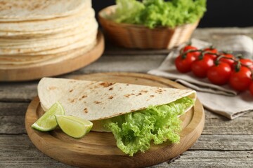 Tasty homemade tortillas, lettuce, lime and tomatoes on wooden table