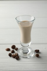 Coffee cream liqueur in glass and beans on white wooden table