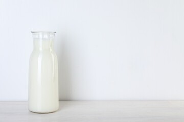 Glass carafe of fresh milk on wooden table, space for text