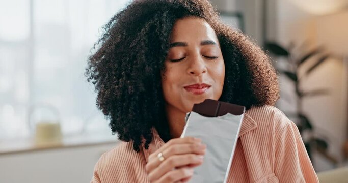 Black woman, chocolate and eating on sofa with smile for satisfaction, snack and craving in house. African girl, dessert and happy in home living room on couch for candy, sweets and sugar food