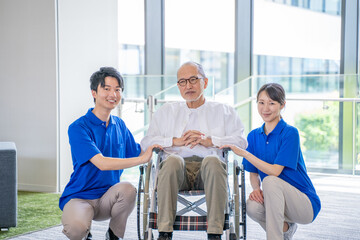 介護施設の車いすに乗ったシニア男性と男女スタッフ