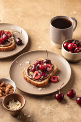 Breakfast toast with chocolate paste, sweet cherry and almond petals on beige textured background. Breakfast for kids
