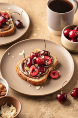 Breakfast toast with chocolate paste, sweet cherry and almond petals on beige textured background close up. Breakfast for kids