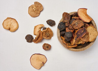 Dried apple pieces in a wooden round plate on a white table, top view