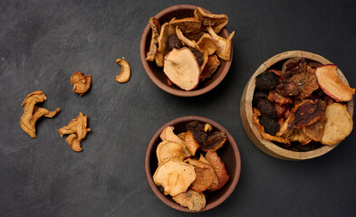 Dried apple pieces in a wooden round plate on a black table, top view