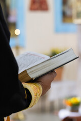 Priest with holy book in his hands against icons. Close up, selective focus.
